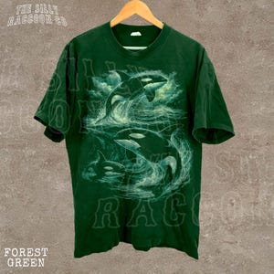 A green t-shirt with a graphic design depicting two orca whales in the ocean.
