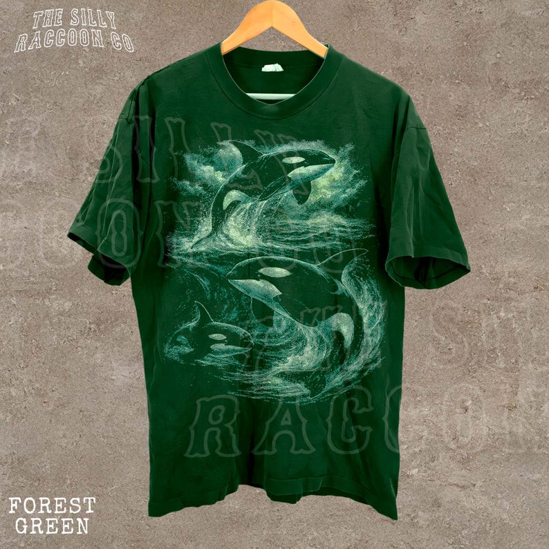 A green t-shirt with a graphic design depicting two orca whales in the ocean.