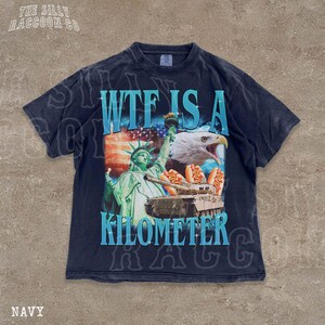 A navy blue t-shirt with a graphic design featuring the Statue of Liberty, an eagle, and hot dogs, along with the text "WTF IS A KILOMETER" and "NAVY".