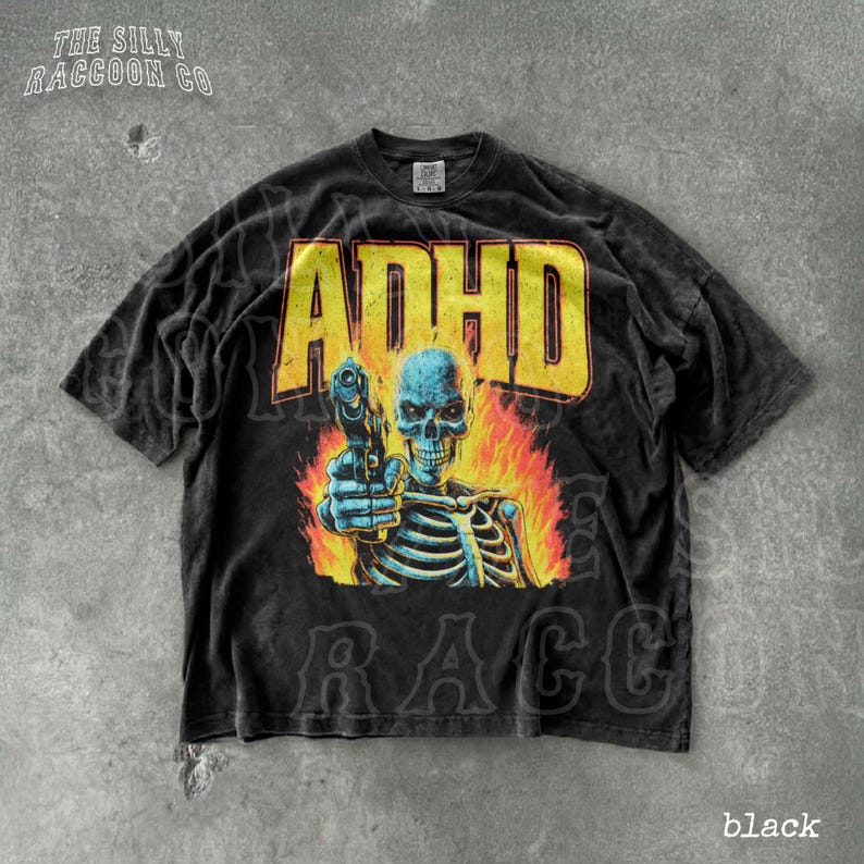 A black t-shirt with a graphic design featuring a skeleton holding a gun and flames behind it.