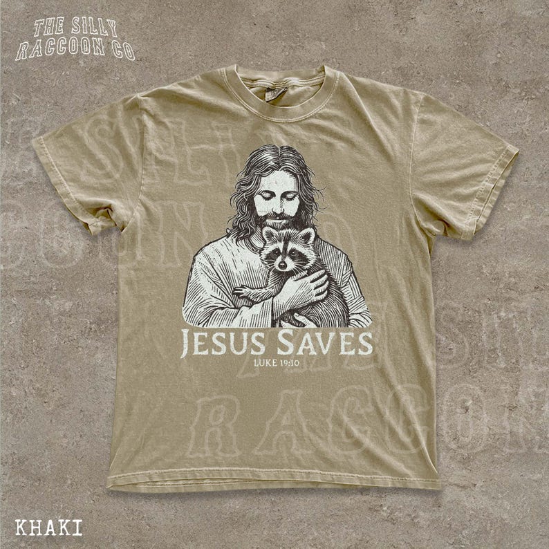 A t-shirt with a graphic design depicting a man holding a raccoon, along with the text "JESUS SAVES LUKELINE 1910" printed on it.