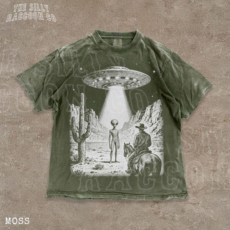 A t-shirt with a graphic design depicting an alien spacecraft hovering over a desert landscape, with a cowboy on a horse below.