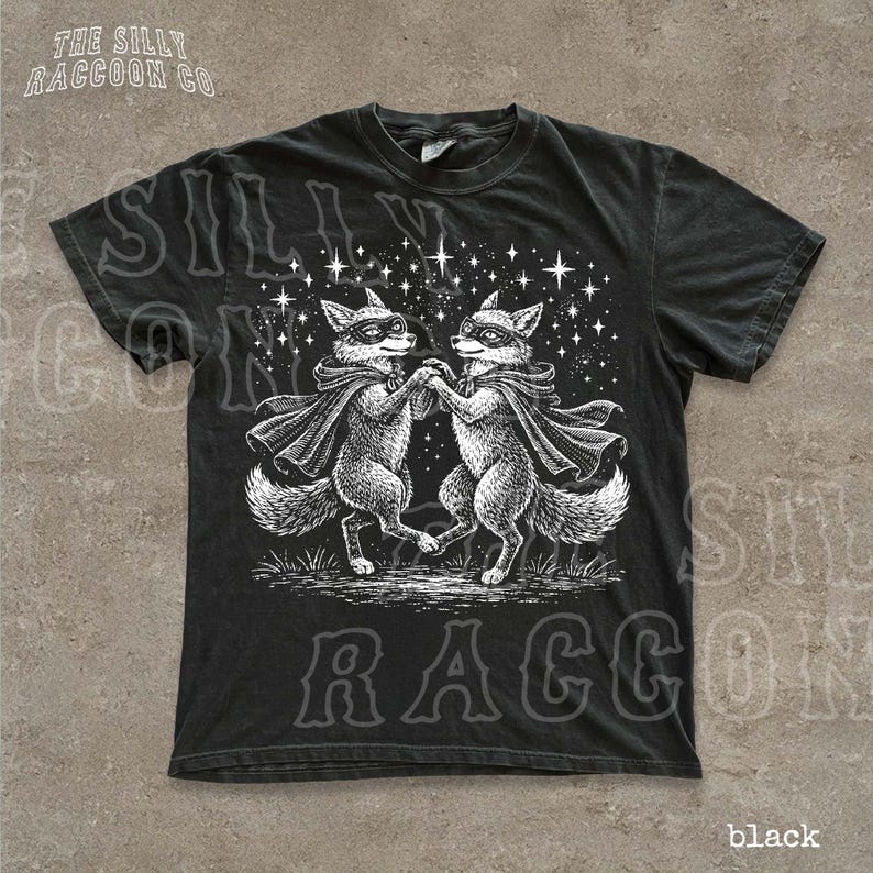 A black t-shirt with a graphic design featuring two foxes dancing under a starry sky.