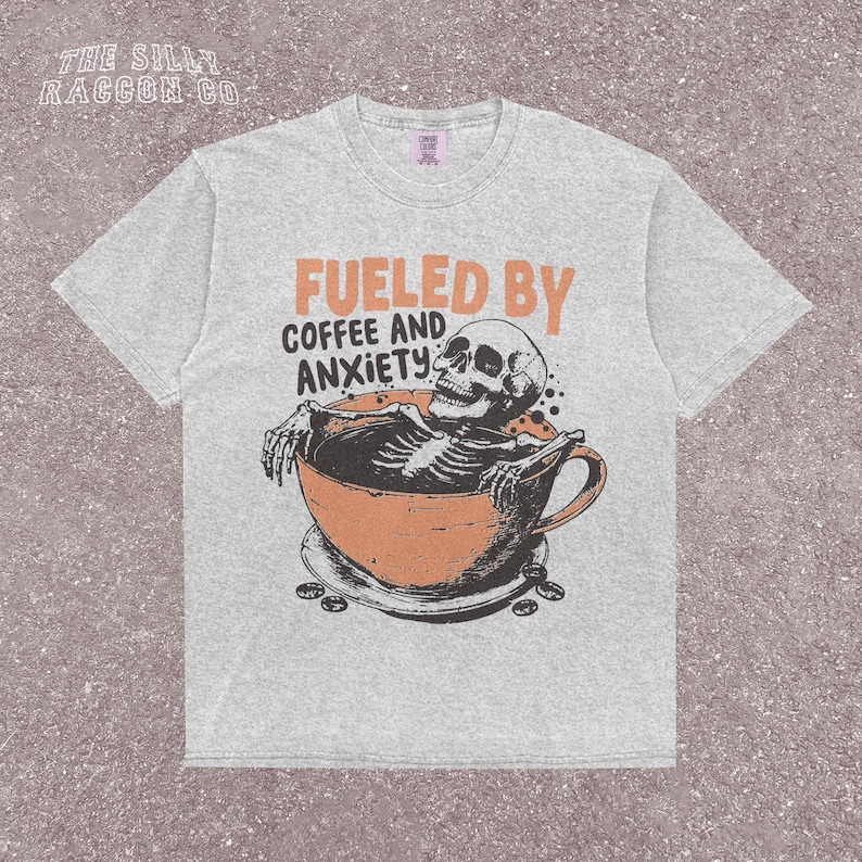 Funny coffee shirt for anxious introverts, featuring a skeleton relaxing in a giant coffee cup with the text “Fueled by Coffee and Anxiety.” Vintage grunge design with distressed print and muted tones. Ideal for women, men, and non-binary adults who love dark humor and caffeine culture. Great for Halloween, work-from-home vibes, mental health awareness, or gifting your favorite goth coffee lover.