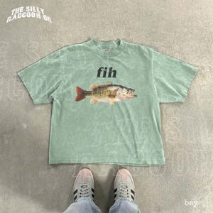 A green t-shirt with a fish graphic and the word 'fih' printed on it, along with a pair of white sneakers.