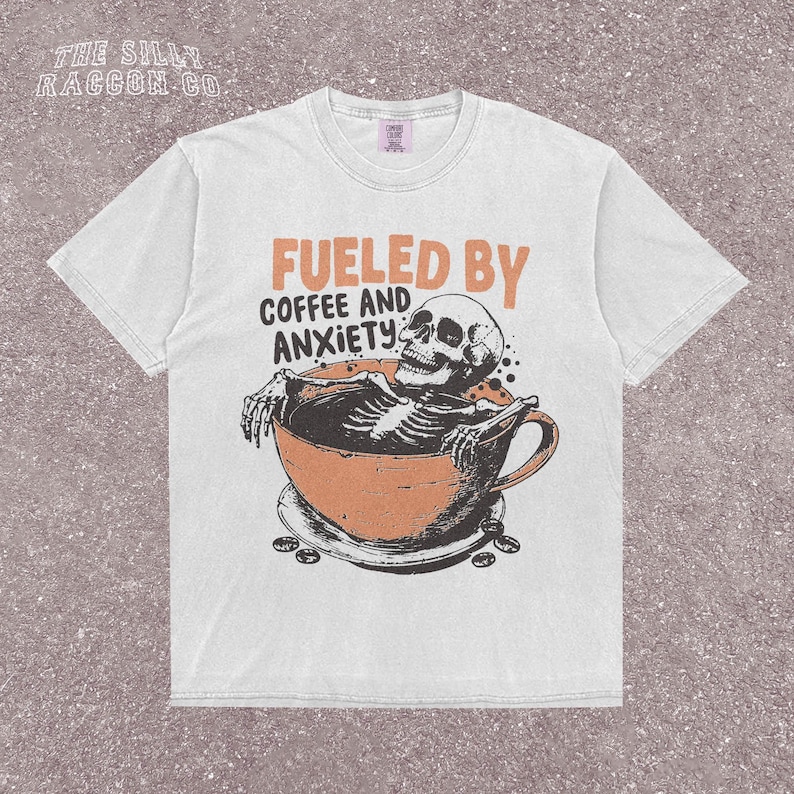 Funny coffee shirt for anxious introverts, featuring a skeleton relaxing in a giant coffee cup with the text “Fueled by Coffee and Anxiety.” Vintage grunge design with distressed print and muted tones. Ideal for women, men, and non-binary adults who love dark humor and caffeine culture. Great for Halloween, work-from-home vibes, mental health awareness, or gifting your favorite goth coffee lover.