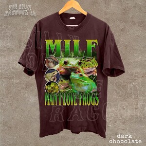 A brown t-shirt with a graphic design featuring a frog and the text "MILF MAN I LOVE FROGS" printed on it.