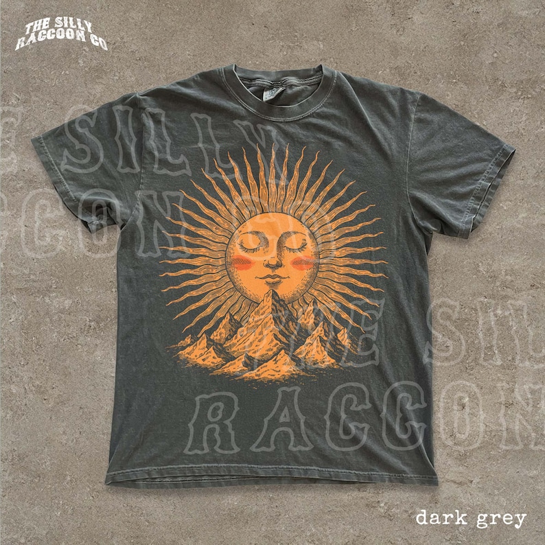 A dark grey t-shirt with a graphic design depicting a sun with rays emanating from it, surrounded by mountains.