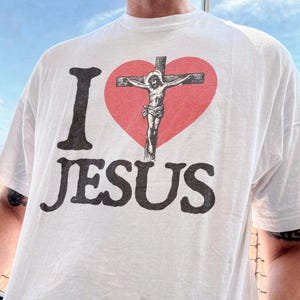 A person wearing a white t-shirt with the text "I ♥ JESUS" printed on it.