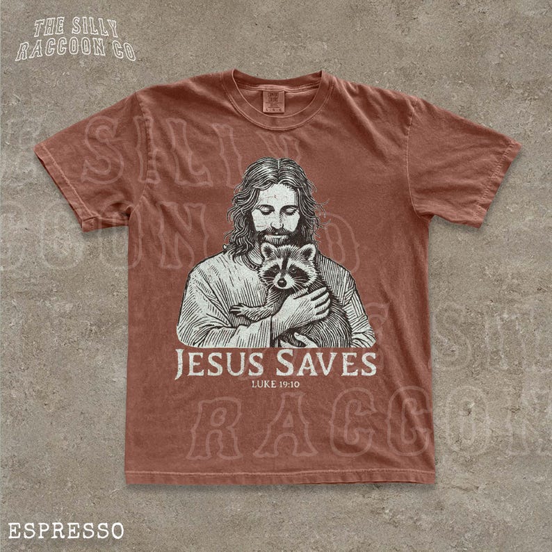 A t-shirt with a graphic design depicting a man holding a raccoon, along with the text "JESUS SAVES" and "LIKE 19:10".