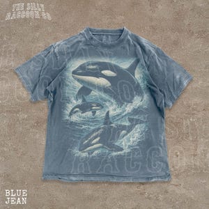 A blue t-shirt with a graphic of two orca whales in the ocean printed on it.