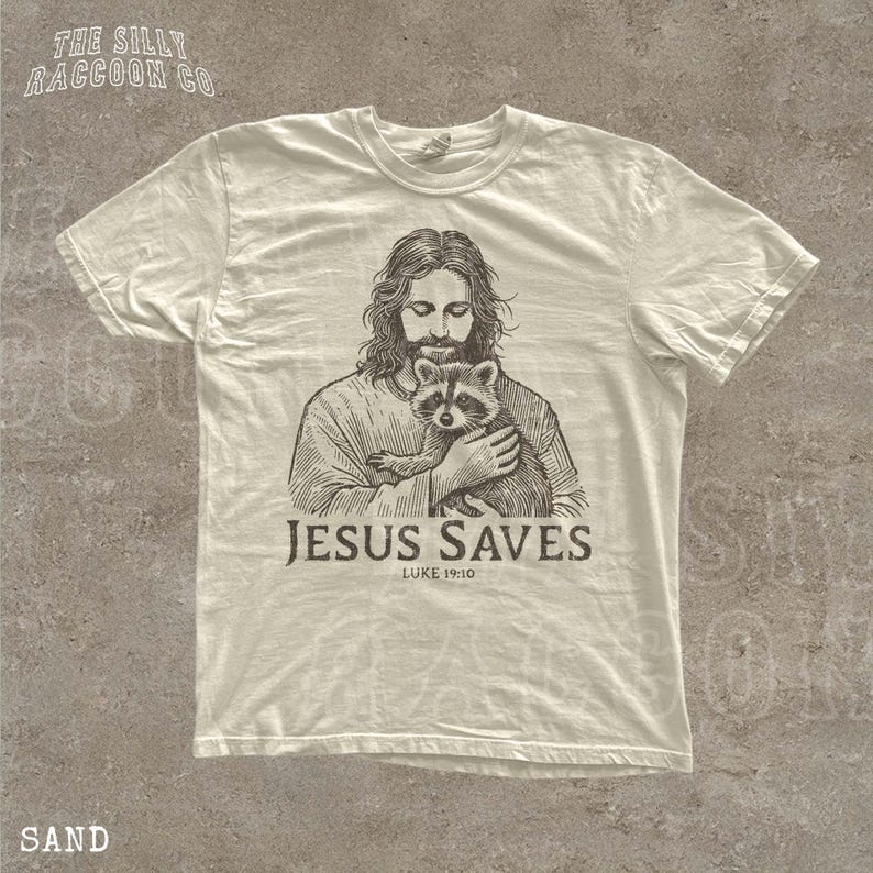 A t-shirt with a graphic design depicting a man holding a raccoon, along with the text "JESUS SAVES" and "LUKELI 19:10".