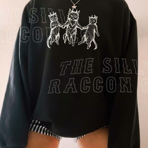 A person wearing a black sweatshirt with a graphic design featuring three cats.