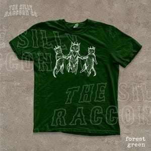 A green t-shirt with a graphic design featuring three cartoon cats with horns.