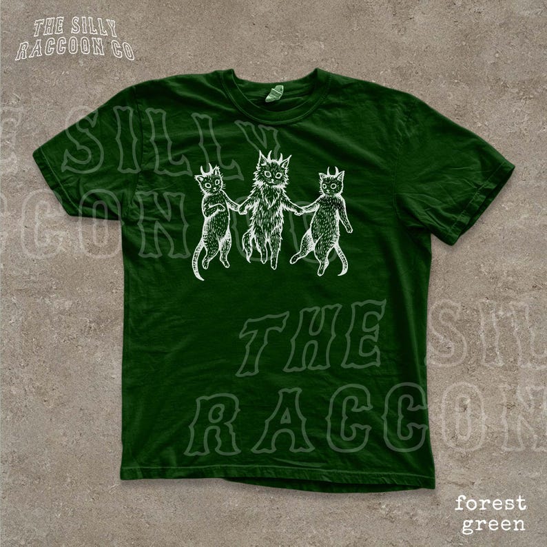 A green t-shirt with a graphic design featuring three cartoon cats with horns.