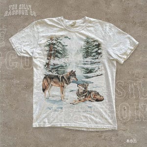 A white t-shirt with a printed design depicting two wolves in a snowy forest setting.