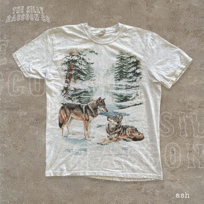 A white t-shirt with a printed design depicting two wolves in a snowy forest setting.