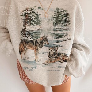 A person wearing a gray sweatshirt with a printed image of two wolves in a snowy forest.