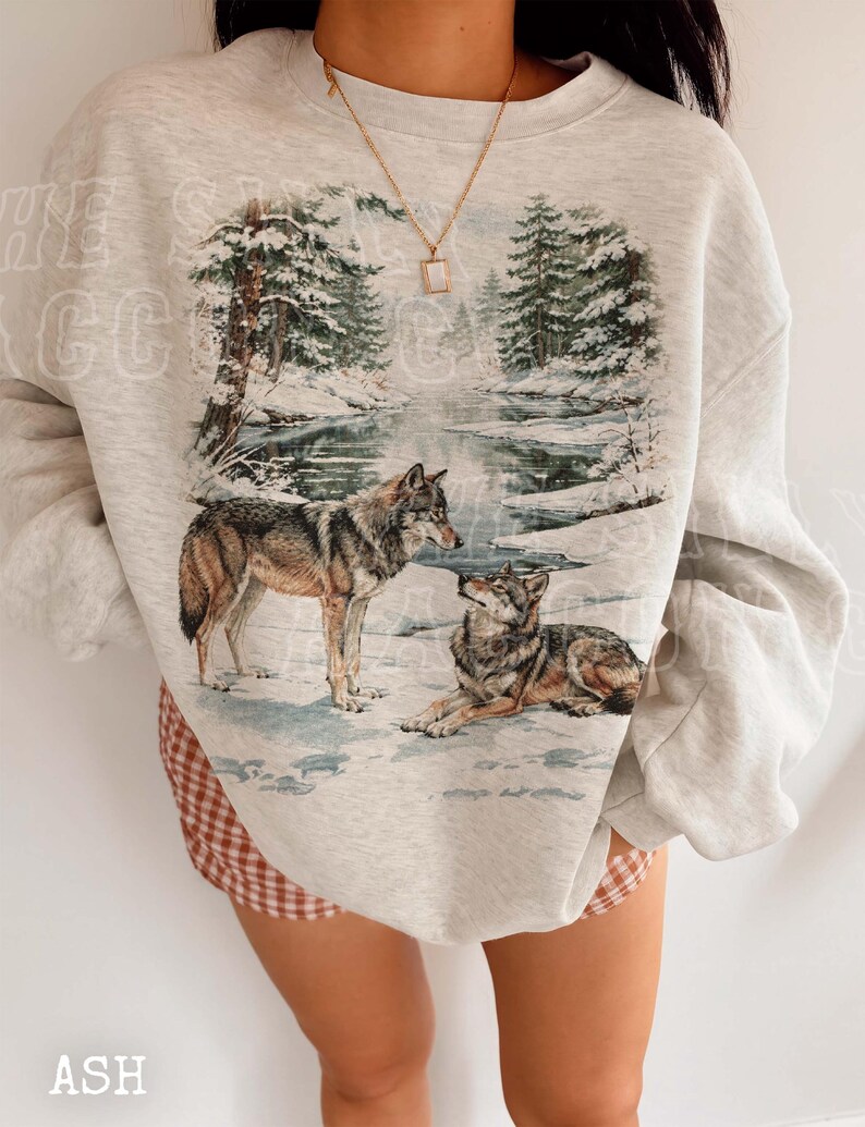 A person wearing a gray sweatshirt with a printed image of two wolves in a snowy forest.