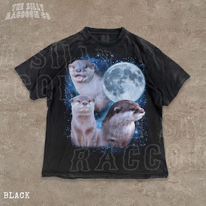 A black t-shirt with a graphic design featuring three otters against a backdrop of a full moon and stars.