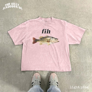 A pink t-shirt with a fish graphic and the word 'fih' printed on it, along with a pair of white sneakers.
