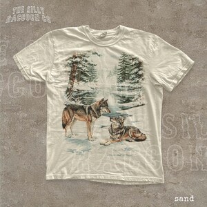 A white t-shirt with a printed design depicting two wolves in a snowy forest landscape.