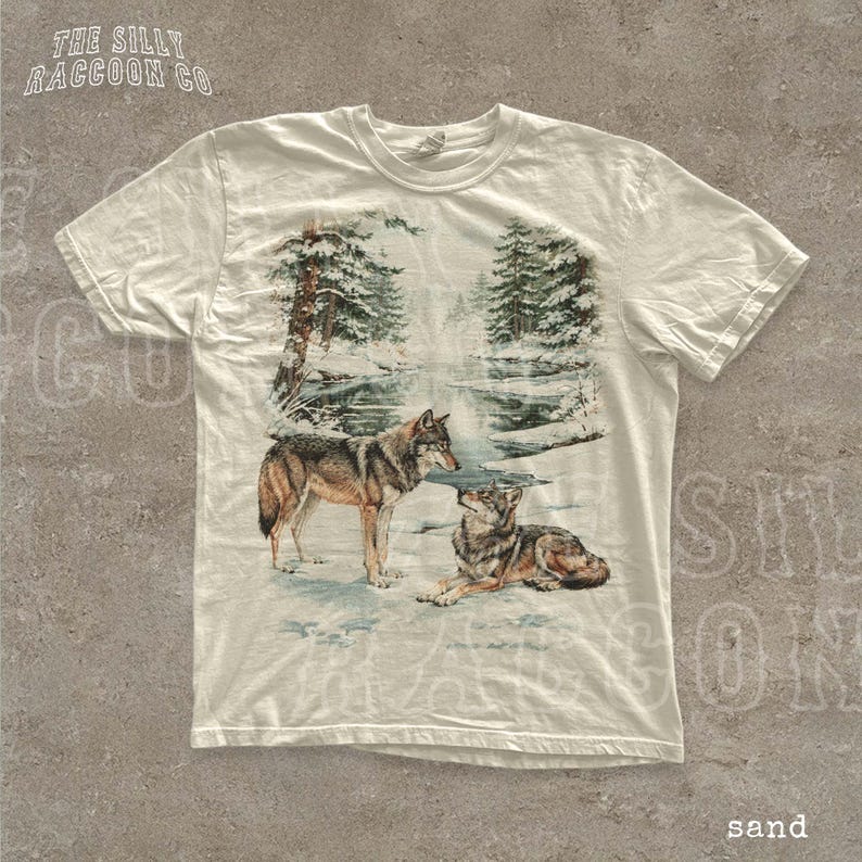 A white t-shirt with a printed design depicting two wolves in a snowy forest landscape.