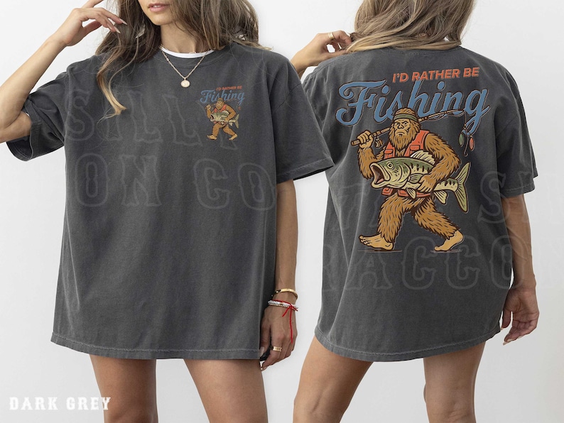 a woman wearing a grey t-shirt with a graphic design on the back. The design depicts a man holding a fishing rod and a fish, with the text "I'd rather be fishing" written above the image.