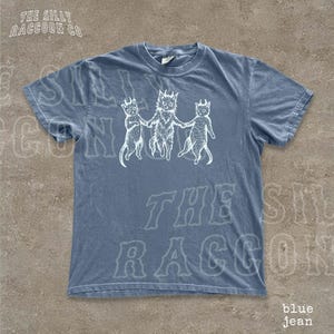 A blue t-shirt with a graphic design featuring three cartoon cats holding hands.