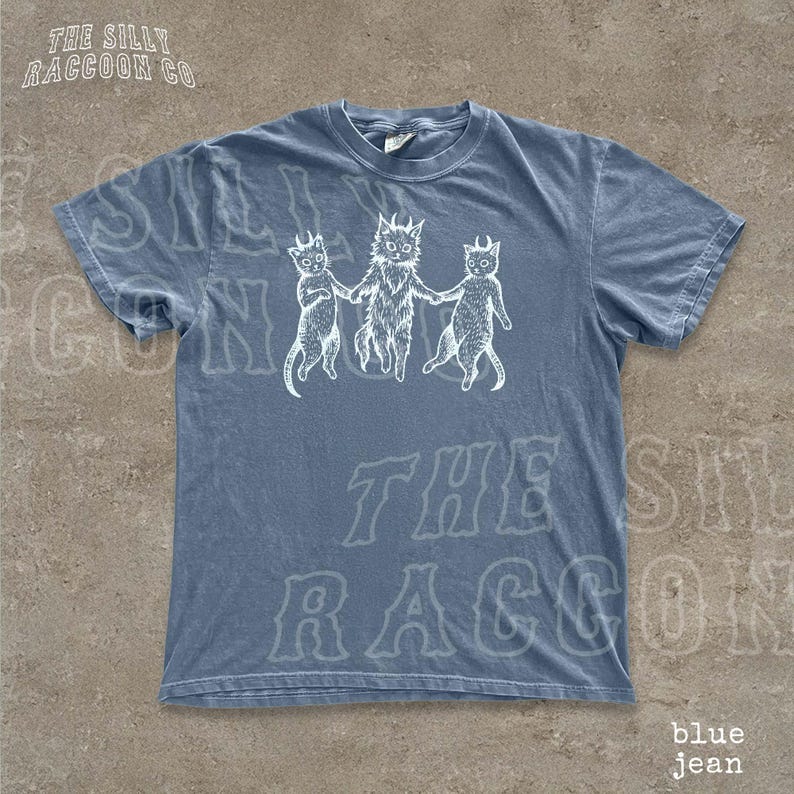 A blue t-shirt with a graphic design featuring three cartoon cats holding hands.