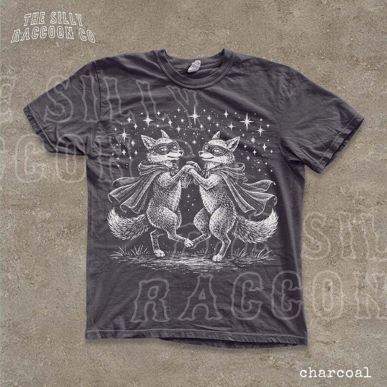 A gray t-shirt with a graphic design depicting two foxes dancing under a starry sky.