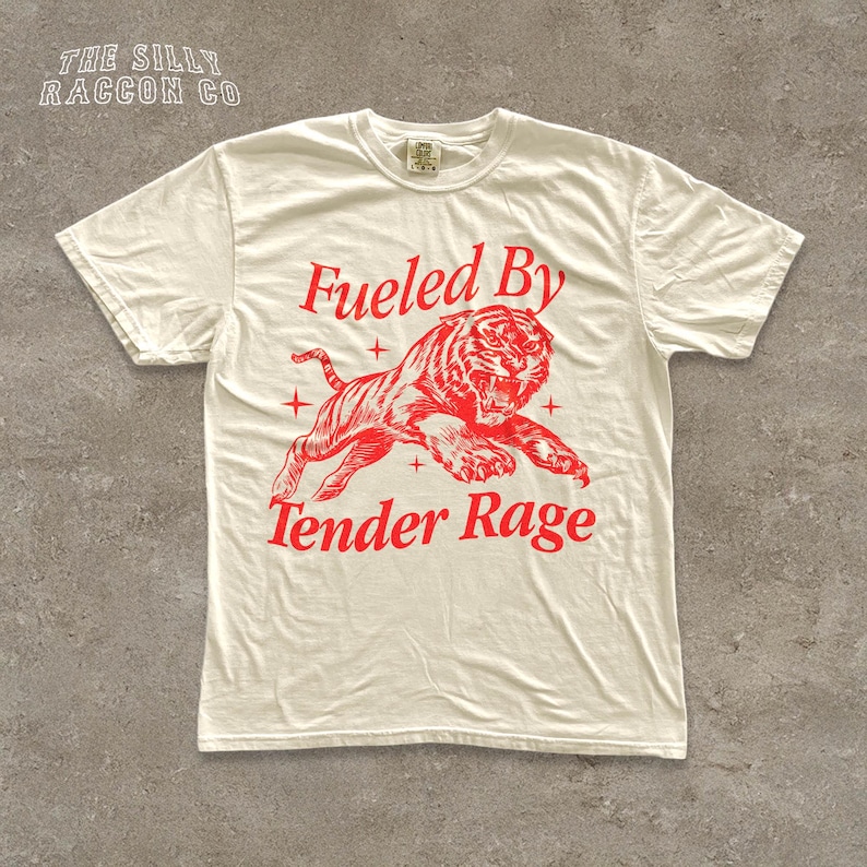 A white t-shirt with a red graphic design depicting a tiger and the text "Fuelled By Tender Rage" printed on it.