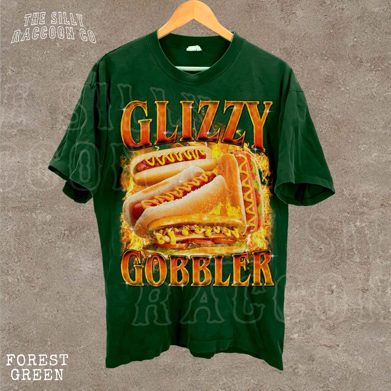 A green t-shirt with a graphic design featuring two hot dogs on a bun, with flames or fire around them, and the text "GLIZZY GOBBLER" prominently displayed.