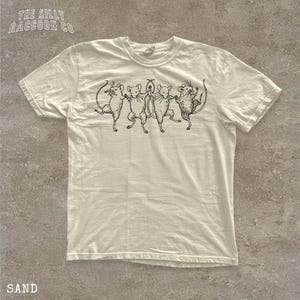 A white t-shirt with a graphic design of five mice dancing together.