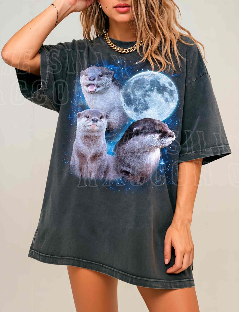 A woman wearing a black t-shirt with a graphic design featuring three otters against a backdrop of a full moon and stars.