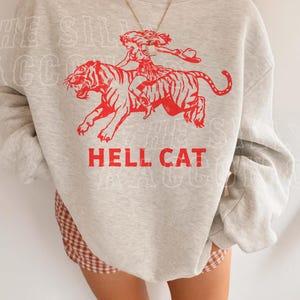 A person wearing a grey sweatshirt with a red graphic design depicting a person riding a tiger.
