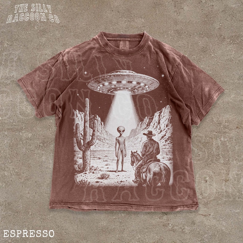 The image is a t-shirt design featuring an illustration of an alien spacecraft hovering over a desert landscape, with a cowboy on a horse below.