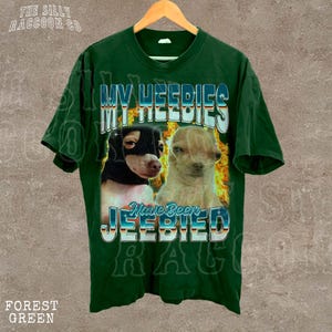 A green t-shirt with a graphic design featuring two dogs, one black and one tan, along with the text "MY HEEDIES" and "Have Been JEEBIED" printed on it.