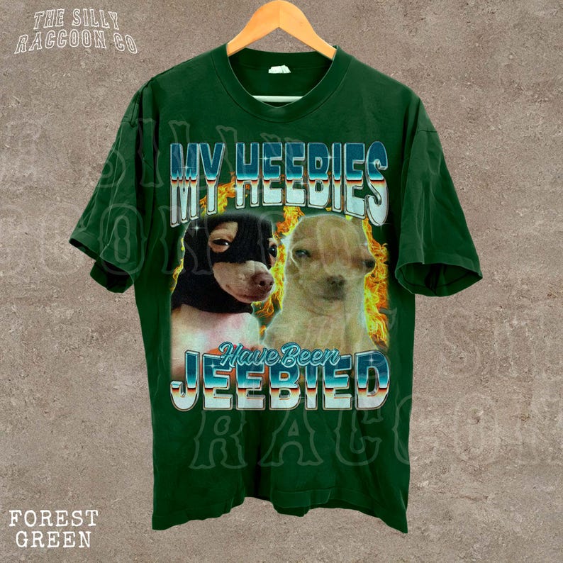 A green t-shirt with a graphic design featuring two dogs, one black and one tan, along with the text "MY HEEDIES" and "Have Been JEEBIED" printed on it.