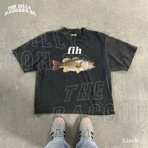 A black t-shirt with a fish graphic and the word 'fih' printed on it, along with a pair of white sneakers.