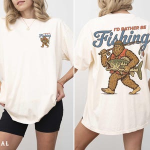 A woman wearing a white t-shirt with a graphic design of a fishing giant on the back.