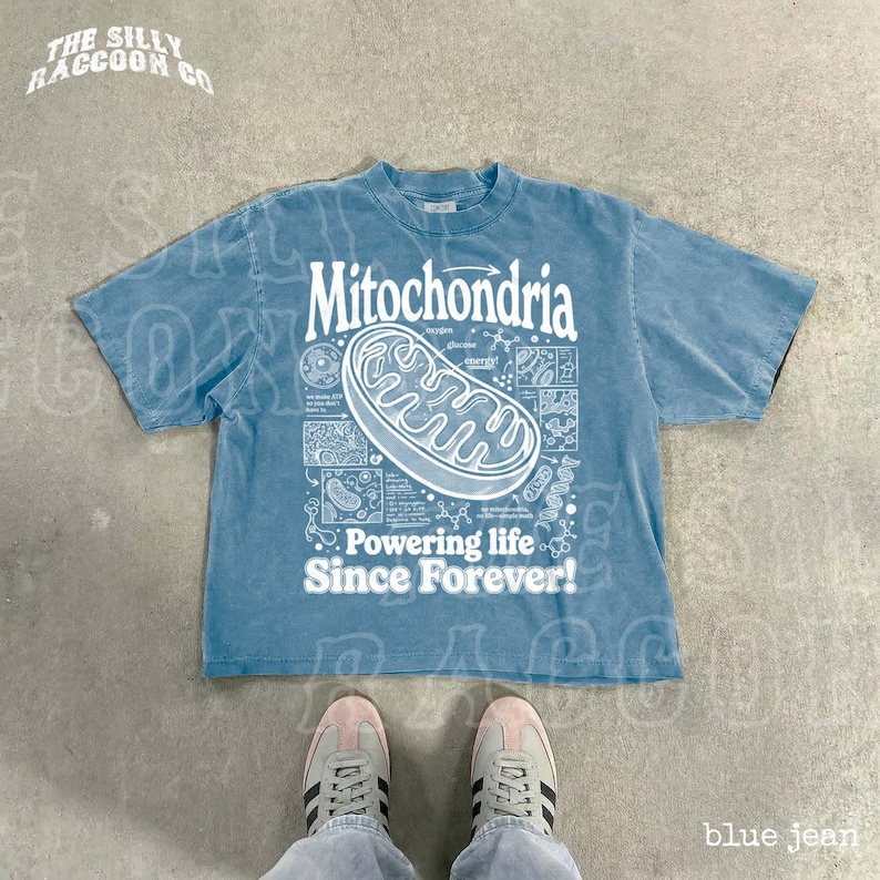 A blue t-shirt with a graphic design and text, along with a pair of sneakers, is displayed on a concrete floor.