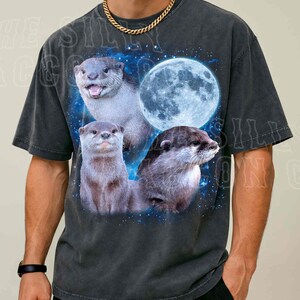 A man wearing a black t-shirt with a graphic design featuring three otters against a backdrop of a full moon and stars.