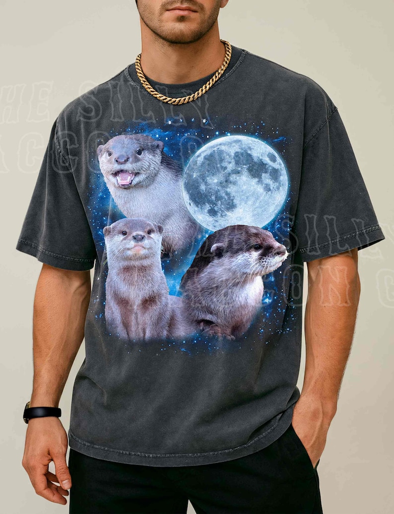 A man wearing a black t-shirt with a graphic design featuring three otters against a backdrop of a full moon and stars.