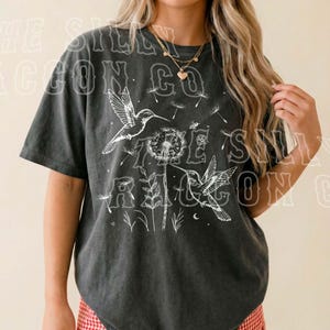 A woman wearing a black t-shirt with a graphic design of birds and flowers, standing against a plain background.