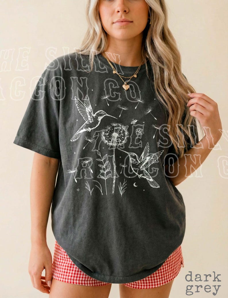 A woman wearing a black t-shirt with a graphic design of birds and flowers, standing against a plain background.