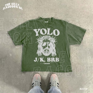 A pair of sneakers and a green t-shirt with a graphic design featuring a man's face wearing sunglasses and a crown, along with the text "YOLO J.K. BRB Jesus".