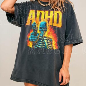 A woman wearing a black t-shirt with a graphic design featuring a skeleton holding a gun and flames.