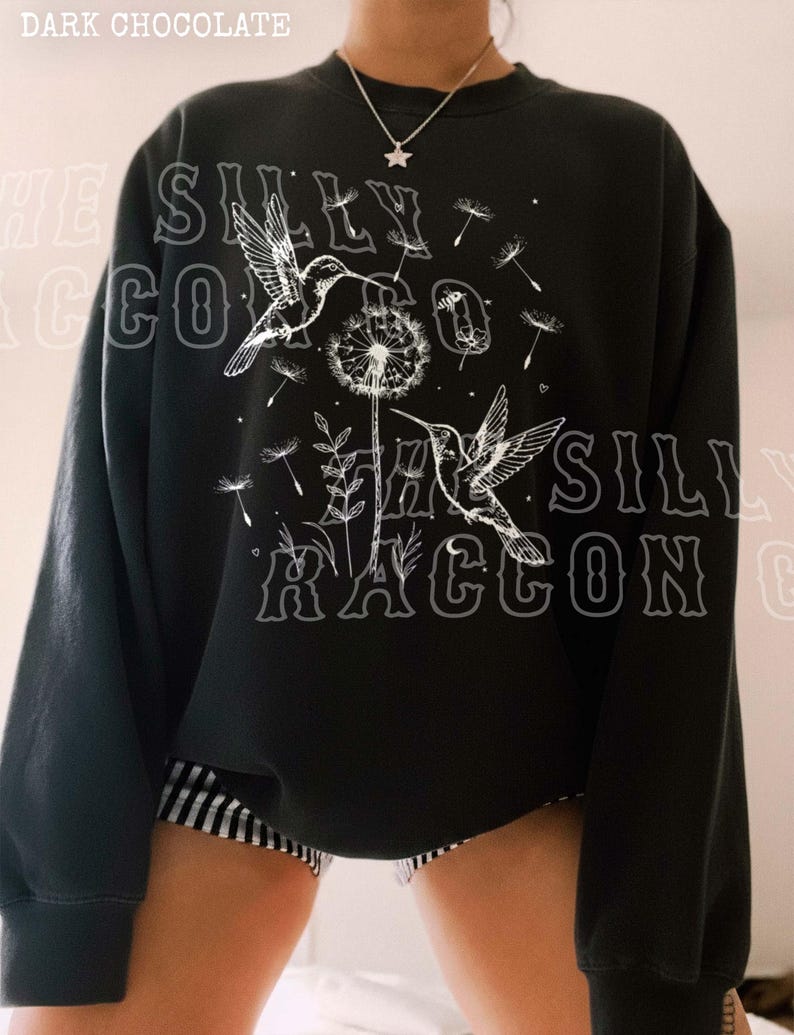 A person wearing a black sweatshirt with a graphic design featuring a bird and a dandelion.