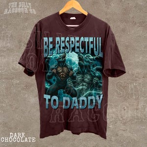 A dark brown t-shirt with a graphic design featuring two werewolves and the text "BE RESPECTFUL TO DADDY" printed on it.
